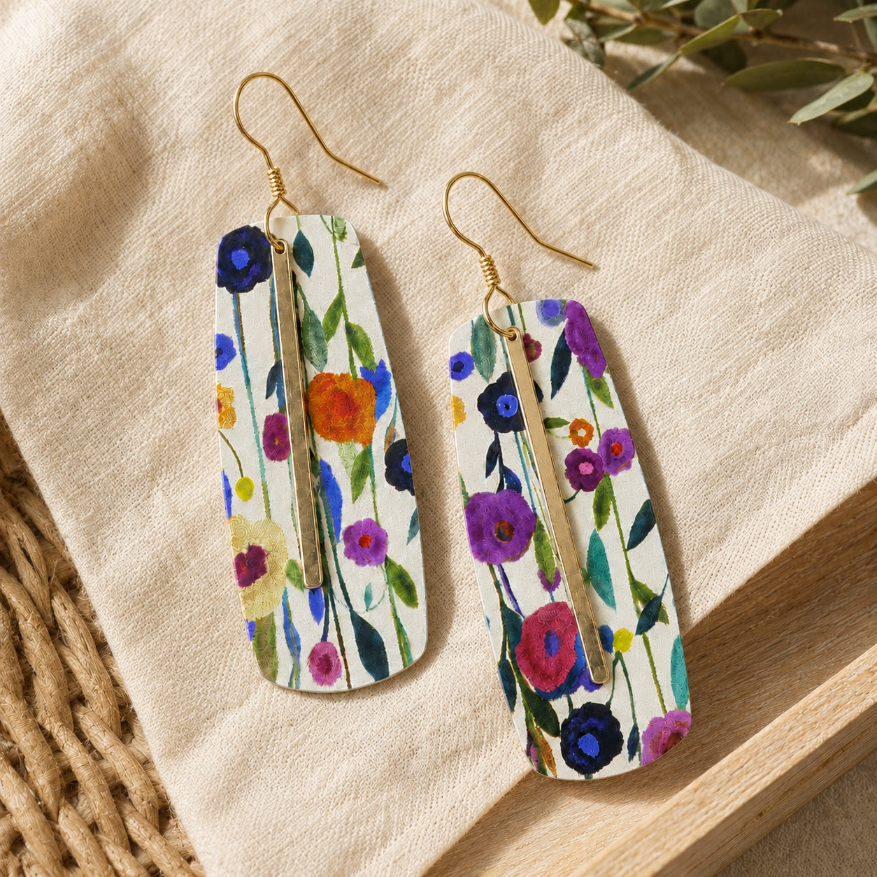 Colorful floral bar earrings with gold hooks and center accents on cream linen.