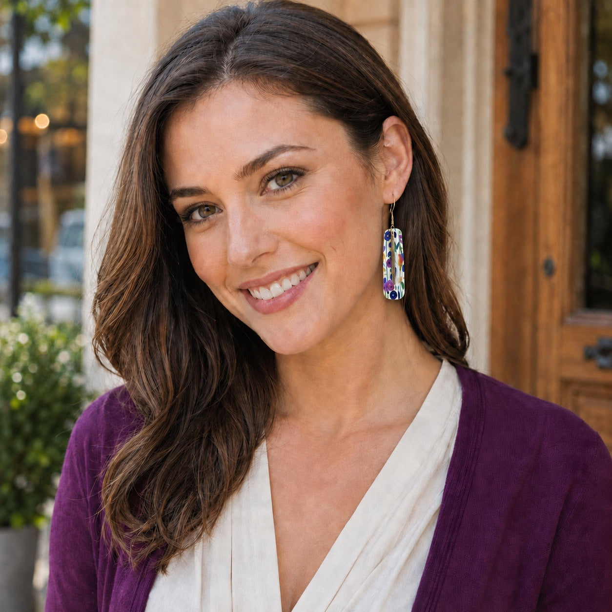 Woman wearing colorful floral bar earrings with an ivory blouse and plum cardigan.