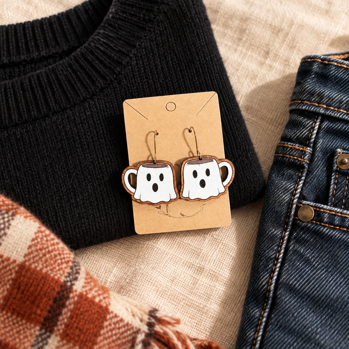 Hand-painted ghost mug wood earrings styled with a black sweater, dark denim, and a plaid scarf