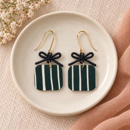 Hunter green striped bow earrings with gold hooks on a cream ceramic dish.