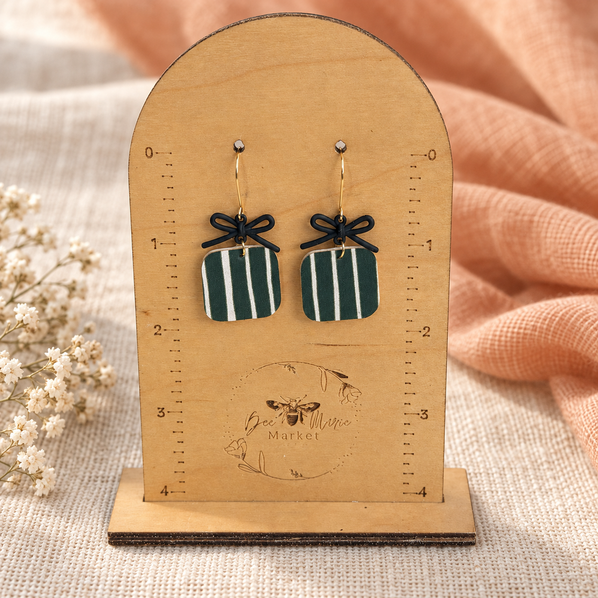 Hunter green striped bow earrings displayed on a wooden measuring stand.