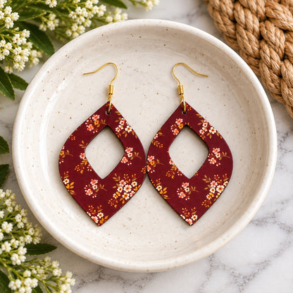 Maroon floral open teardrop earrings with gold hooks in a cream dish