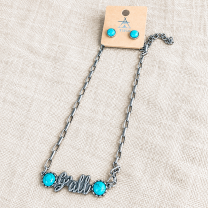 Silver y'all necklace and turquoise stud earrings on cream linen