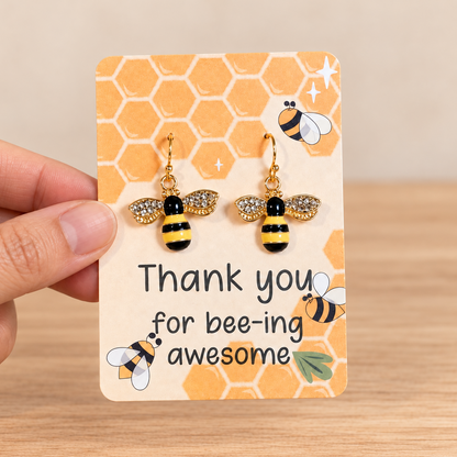 Natural hand holding sparkling black and yellow bee earrings against a simple neutral background