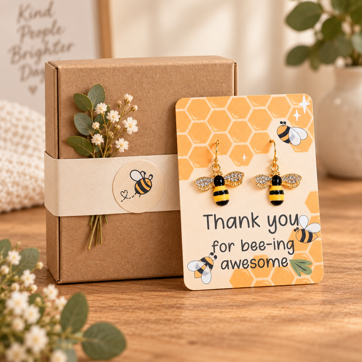 Sparkling bee earrings on a card leaning against a closed kraft gift box