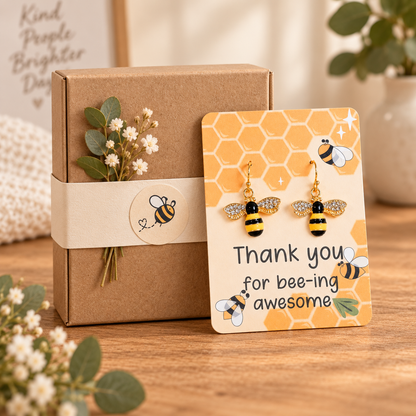 Sparkling bee earrings on a card leaning against a closed kraft gift box