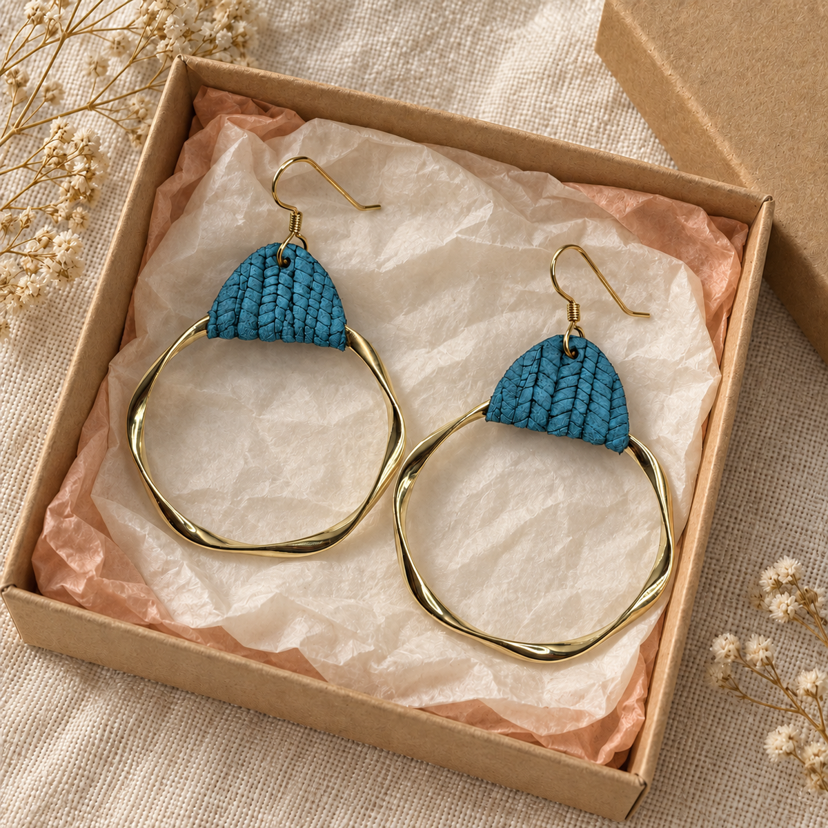 Teal leather and twisted gold hoop earrings styled in a kraft gift box.
