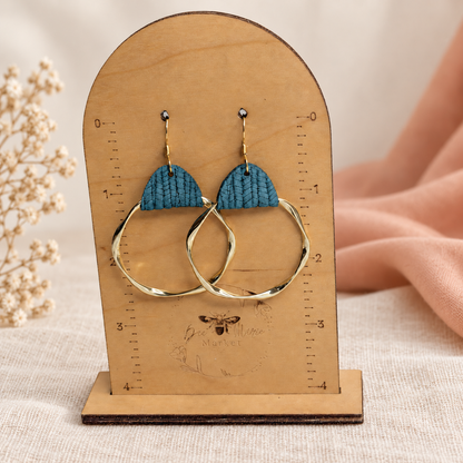 Teal leather twisted gold hoop earrings displayed on a measuring stand.