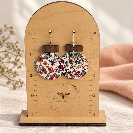 Round floral cork on leather earrings with wood bars shown on a Bee Marie Market measuring stand.